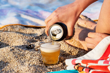 Canned beer pouring into glass on the beach.
