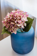 close up of a blue vase with pink flowers on the table