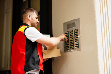 Delivery man pressing button of intercom to enter building
