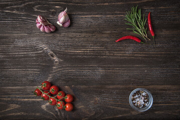 Wooden background with vegetable decor: cherry tomatoes, garlic, rosemary and chilli peppers