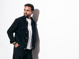 Handsome confident hipster model. Sexy unshaven man dressed in black  summer t-shirt and jeans clothes. Fashion male posing near white wall in studio at sunny day. Isolated