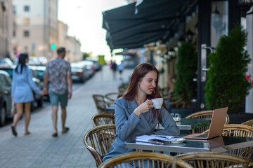 Beautiful professional ht manager woman in a fashion business suit working on a laptop and drinking coffee