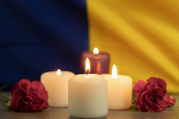 Fototapeta na wymiar A group of burning candles and flowers on the background of the national flag of Ukraine