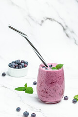 Bilberry smoothie yogurt, fresh blueberries in glass with mint leaf and raw beeries on blue background. Restaurant menu, dieting, cookbook recipe top view