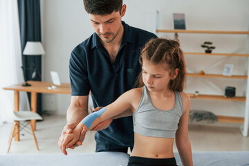 Obraz premium Professional physiotherapist putting kinesio tape on kid arms in clinic