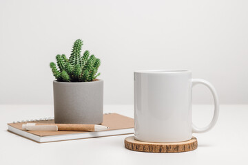 White mockup mug with notepad and cactus  houseplant at the background. Mug with copy space for brand, logo or text, office or education concept