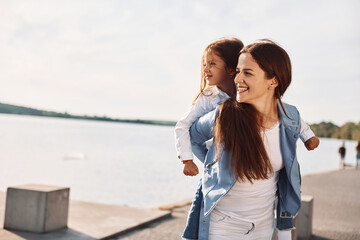 Positive emotions. Young mother with her daughter having fun outdoors near the lake at summer