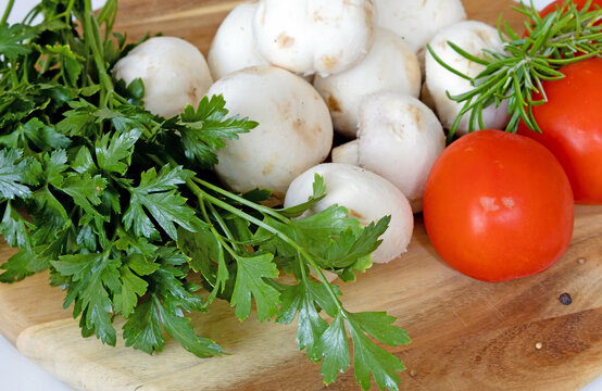 Fresh white champignons mushrooms, tomatoes, parsley and thyme on cutting board. Vegan concept.