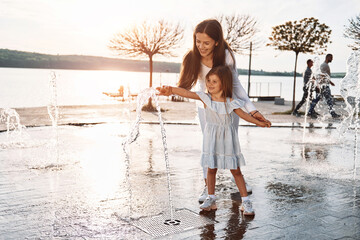 Holding each other. Little girl with her mother having fun outdoors in fountain near the lake