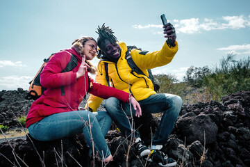 Couple of young hikers sitting on the lava stone taking a selfie snapshot with their smartphone - people and vacation concept