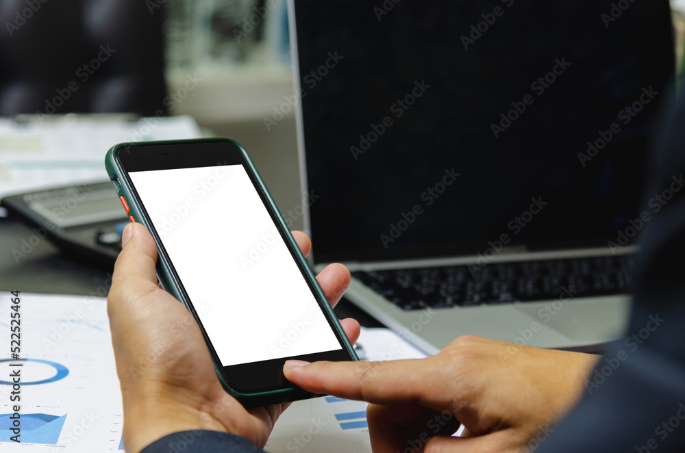 Poster man holding mobile smartphone mock up blank white screen and computer laptop document graph on desk.