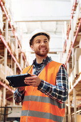With tablet. Employee in uniform is working in the storage at daytime
