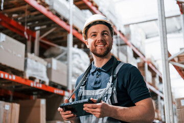 Obraz premium With digital tablet in hands. Employee in uniform is working in the storage at daytime