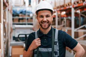 Smiling for the camera. Employee in uniform is working in the storage at daytime