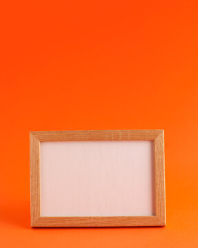 Close up of mockup template white frame with wooden borders on orange blurred background and copy space. Holiday autumn concept backdrop.