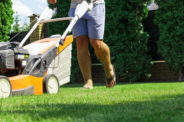 Man mowing the lawn with lawn mower in summer. Spring season sunny lawn mowing in the garden.