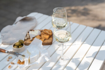 Two glasses of white wine and a wooden plate of cheese and nuts in the backyard.