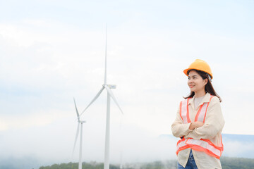 Young woman engineer with windmill at a renewable energy generating station in a windmill field.