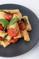 Italian dish. Pasta with cherry tomatoes and basil. Food in a black plate on a white background.
