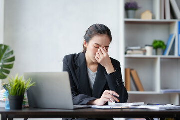 Beautiful Asian businesswoman is tired from working in the office. because of using too much eyes while working on laptop computer in office.