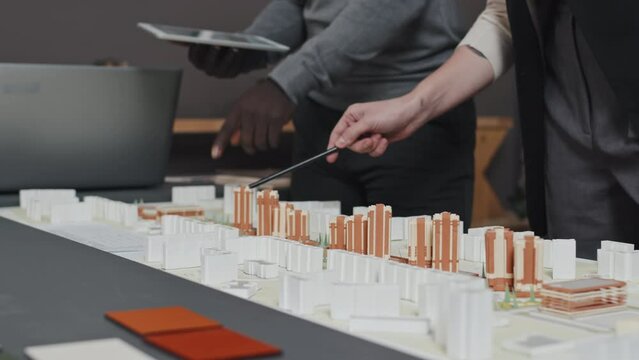 Midsection slow motion of two cropped architects revising city layout on desk in office