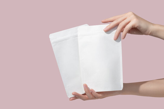 Woman's hands hold cardboard packages for tea or snacks on a pink background. Tea branding and packaging mockup.
