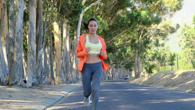 attractive fitness woman wearing tracksuit running outdoors. Happy young attractive woman in sportswear warming up before jogging. athletic thin girl runs through the park near the alley of trees