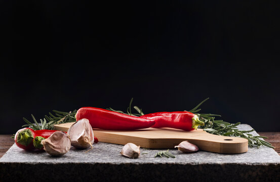 Beautiful red hot pepper, rosemary and garlic on a granite stone. Composition for decoration with the presence of spices and spices. Black background for your dough with elements for cooking.