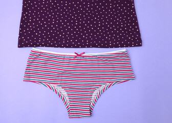 Top view polka dot tank top and striped briefs. Cotton casual panties for women. Women's underwear on a light purple background.