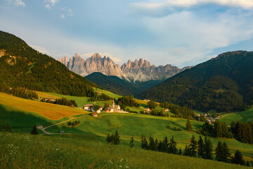Fototapeta na wymiar Stunning view of the Funes Valley (Val di Funes) with the Santa Maddalena Church and the mountain range of the Puez Odle Nature Park in the distance during a beautiful sunset. Santa Magdalena, Italy.