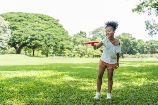Happy African American little girl in curly hair has fun playing with red frisbee in park.kid activity outdoor.