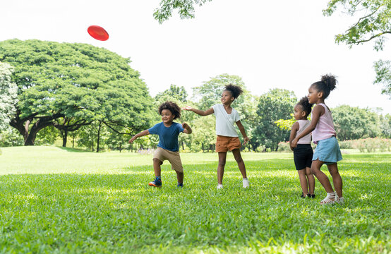 Group African American little girl and boy have fun playing and throwing frisbee in the park.Kids playing games and flying disc on green lawn outdoor.