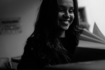 Black and white portrait of a young brunette girl with a book in her hands. Women is siting in the chair 