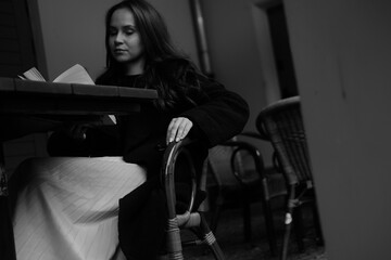 Black and white portrait of a young brunette girl with a book in her hands. Women is siting in the chair 