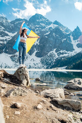 A woman with Ukrainian flag is standing on the shore of a lake. Morskie Oko