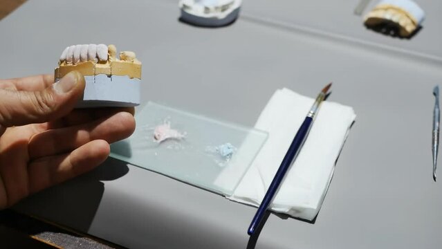 the process of making a denture by a dental technician. The hands of a dental technician holding a brush and a sharp scalpel are shaping artificial teeth. Close-up.