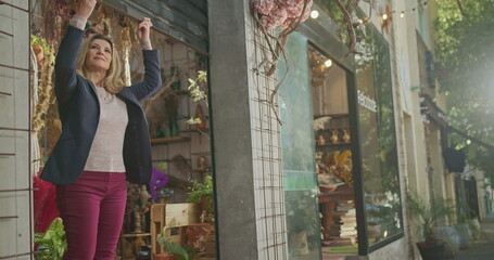 Small business owner opening local store. Female entrepreneur sliding shutters at sidewalk shop. Happy businesswoman opens flower store. Open for business concept