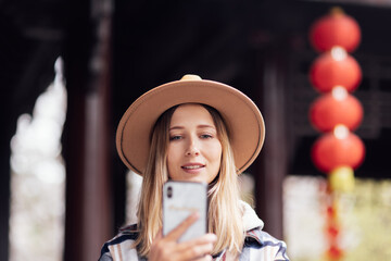 Stylish young caucasian woman 30 years old with blonde hair wearing casual clothing and traveling to China at Autumn. Person using mobile phone outdoor