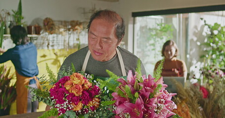 Asian American business entrepreneur owner of flower shop standing holding two bouquet of flower arrangements smiling at camera. Small business concept
