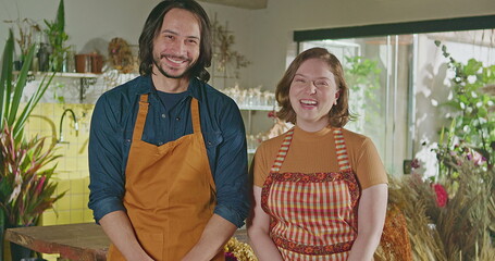 Portrait of two floriculture professionals inside flower shop. Male and female employee staff...