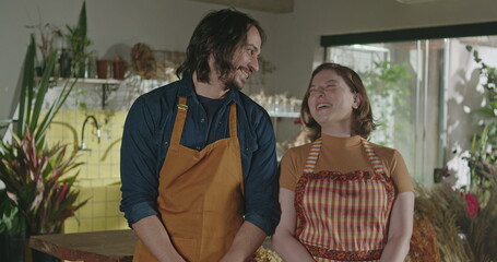 Portrait of two floriculture professionals inside flower shop. Male and female employee staff smiling at camera wearing aprons