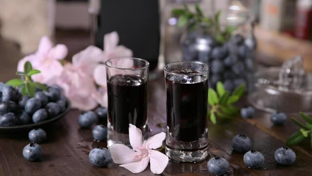 Mirto liqueur. A traditional blueberry liqueur from Sardinia, Italy. Sweet and aromatic drink at the end of the meal. Two small glasses with an alcoholic drink on the table and blueberries. slowmotion