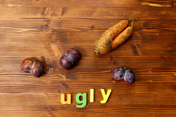 Ugly organic blue plums and carrot on wooden background. The ugly produce trend is the sale of...