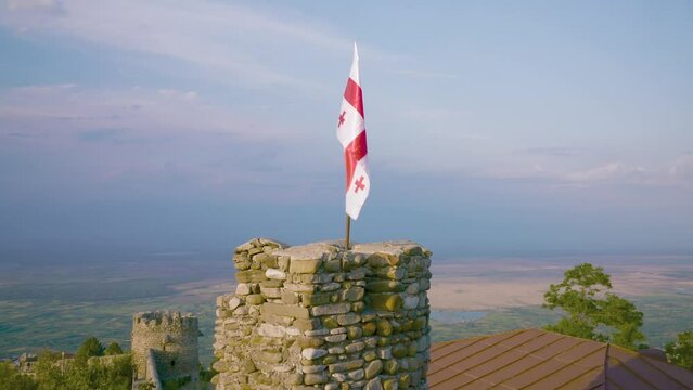 National flag of Georgia waving in wind on medieval fortress of Chailuri against backdrop of a valley. Kakheti Region, Georgia