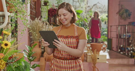 Fototapeta premium Female florist smiling at camera inside flower shop with arms crossed. Portrait of a young woman worker at small business store