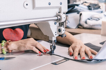 The seamstress sews at the sewing machine, threads the fabric. Women's hands