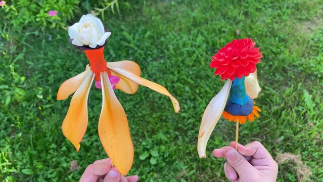 Close-up of children's hands holding dolls made of flower petals and plasticine on a stick. Ideas for a child's creativity in the summer.