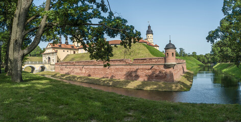 Naklejka premium Moat of old castle. Moat with reflection in the water and trees. Sunny summer day. Palace, tower, corner towers and moat.