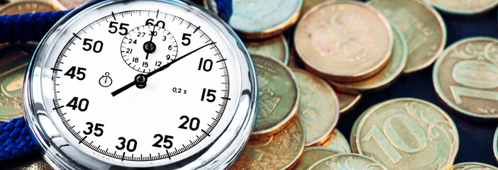 Analog stopwatch and pile of gold coins on a black background close-up. Banner.Counting time by...