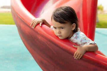 Fototapeta na wymiar Little toddler girl on a red slide, summertime and childhood concept 